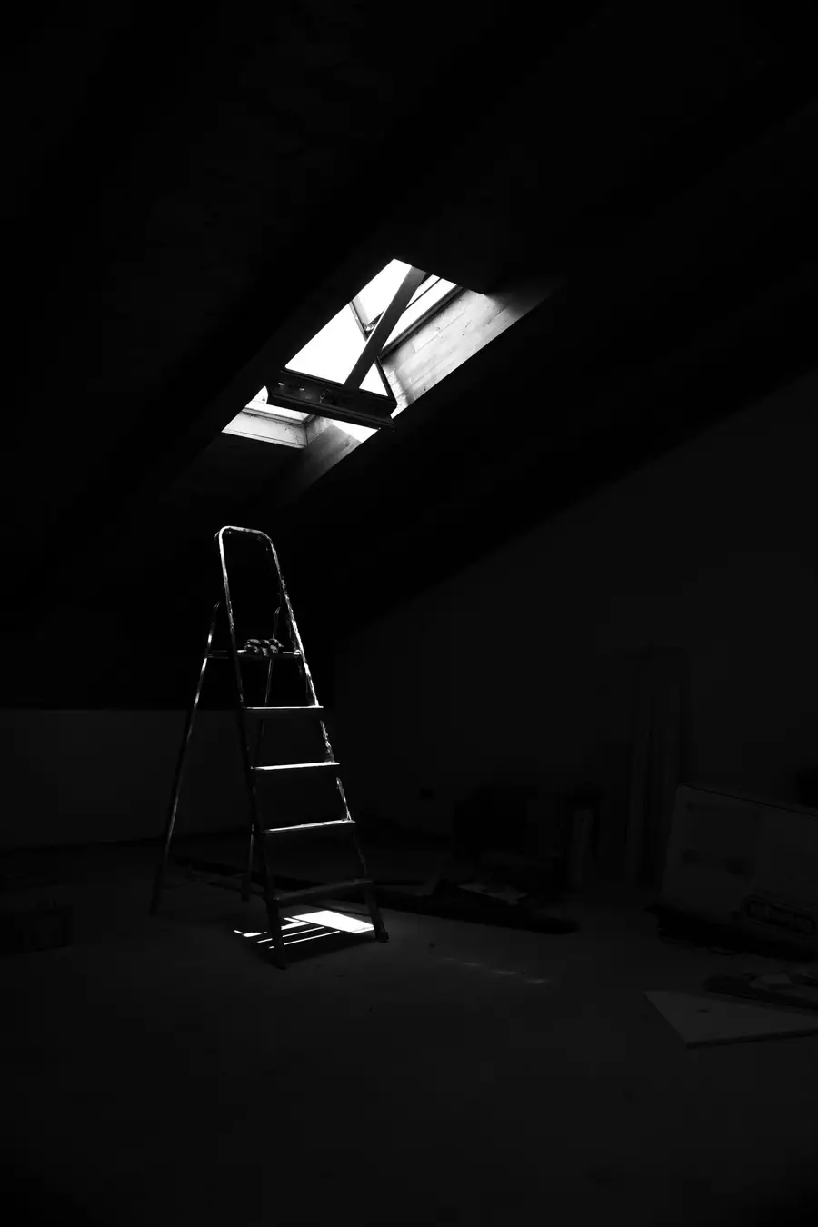 Stepladder in a dark attic beneath a roof window